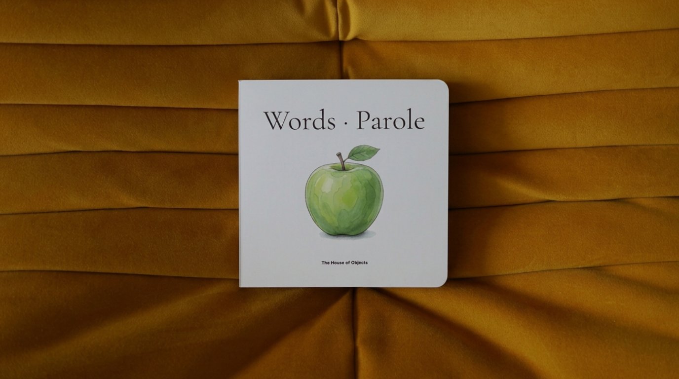 A toddler sitting on a mustard yellow armchair looking at the bilingual board book Words · Parole